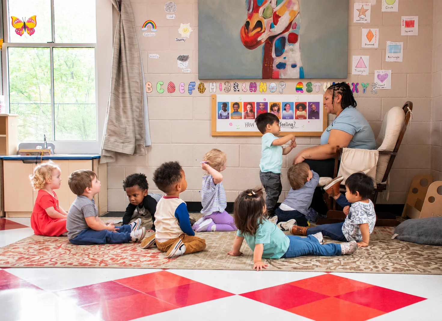 A teacher sitting in a rocking chair reading a book to a group of young children sitting attentively on a colorful patterned rug during storytime.